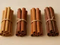 Quatre bouquets de bâtons de cannelle, liés par de la ficelle, sur un fond de bois clair. La cannelle exhale un parfum chaleureux.