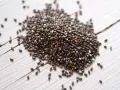 Un tas de graine de chia germé, petites et noires, sur un fond de bois blanc.