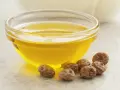 Huile dorée dans un bol en verre, entourée de noix de terre. Découvrez les noix de terre bienfaits pour une peau éclatante et une santé optimale.