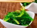 Salade d'algue de mer verte et brillante, servie dans un bol blanc, prête à être dégustée avec des baguettes.