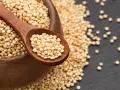 Une cuillère en bois remplie de quinoa cru, posée sur un bol débordant de ces graines nutritives.