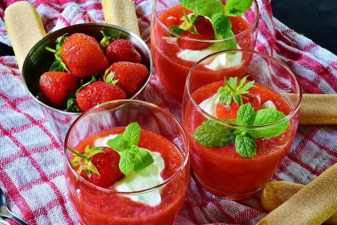 Trois coupes de coulis de fraise, garnies de crème et de menthe, avec des fraises fraîches dans un bol.