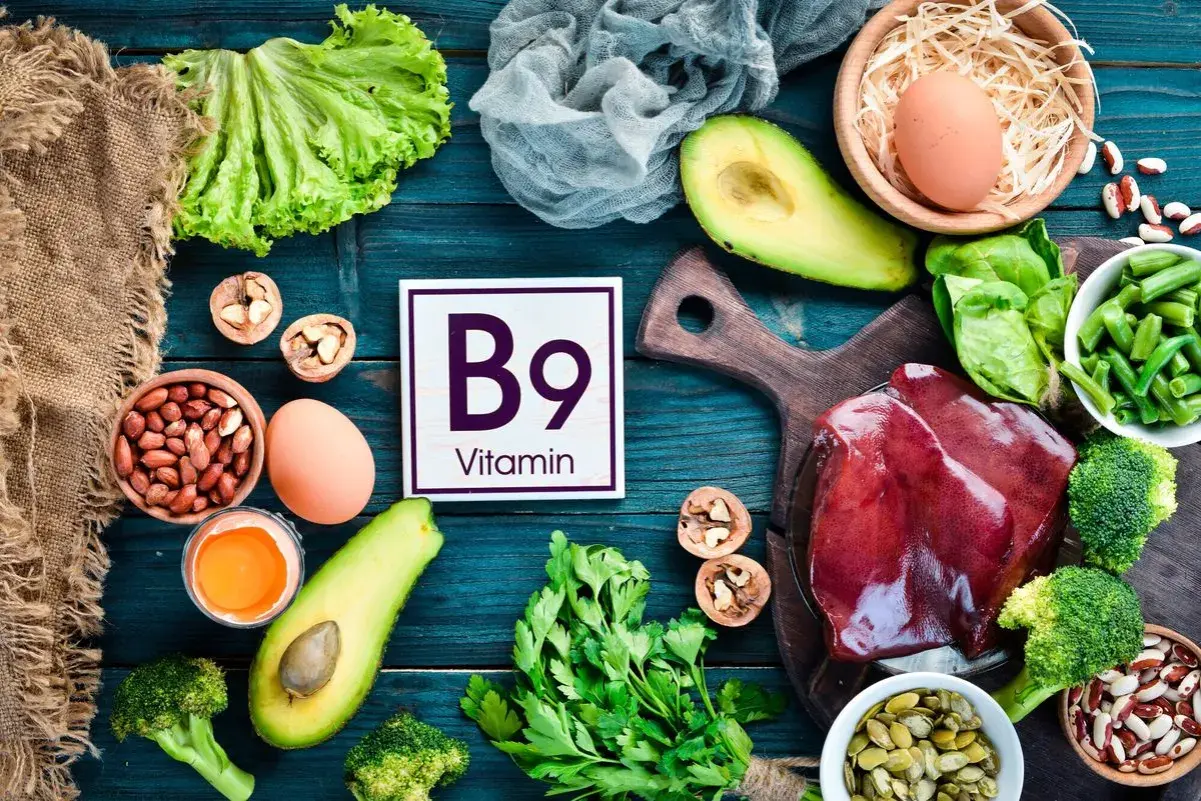Assiette colorée avec foie, légumes verts, avocats, œufs, noix et haricots, mettant en avant la vitamine B9 essentielle.