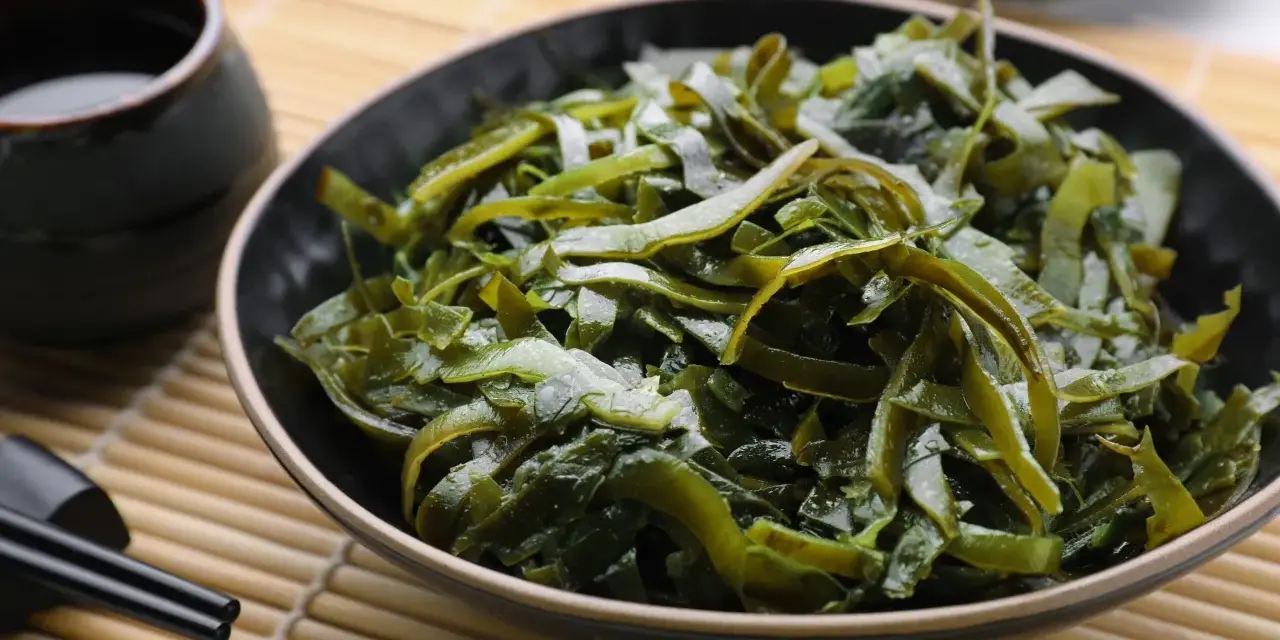 Un bol de salade d'algues kombu, aux multiples algue kombu bienfaits, servi avec une sauce et des baguettes sur un tapis de bambou.