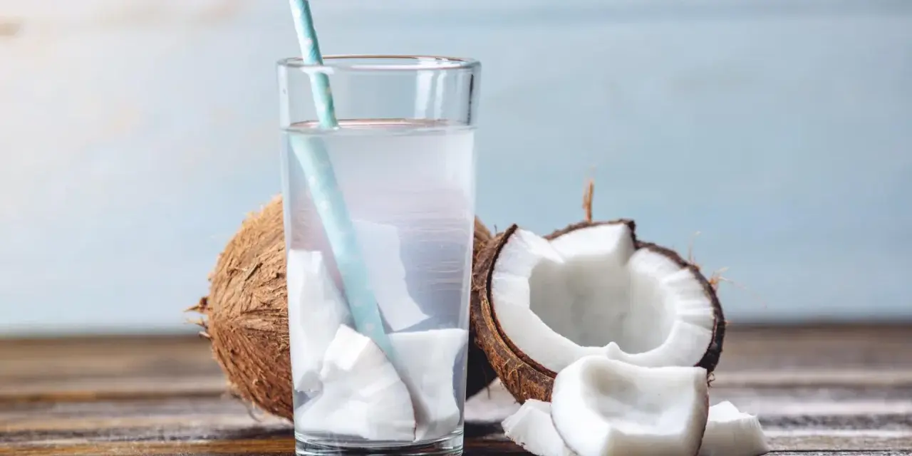 Verre d'eau de coco fraîche avec des morceaux de noix de coco. Une boisson naturelle pour soulager la constipation.