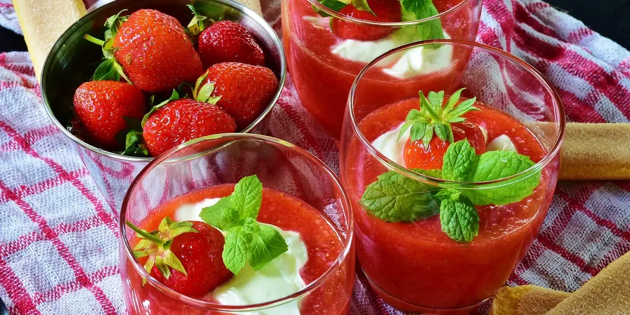 Trois coupes de coulis de fraise, garnies de crème et de menthe, avec des fraises fraîches dans un bol.
