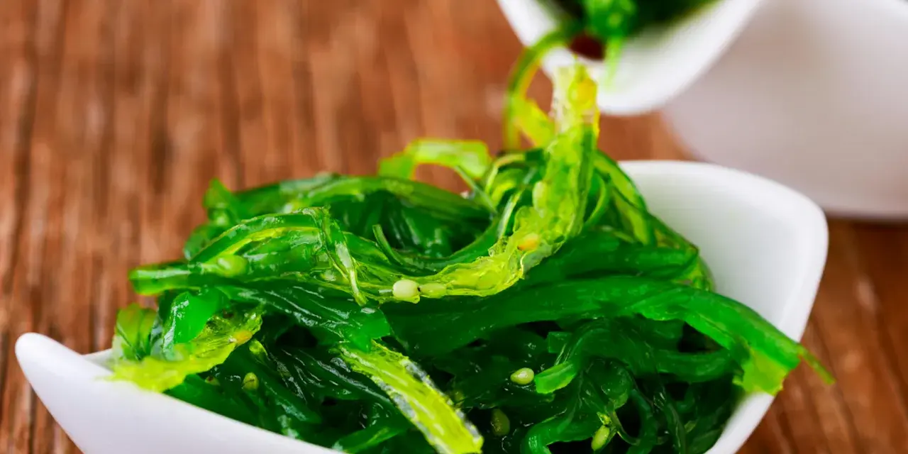 Salade d'algue de mer verte et brillante, servie dans un bol blanc, prête à être dégustée avec des baguettes.