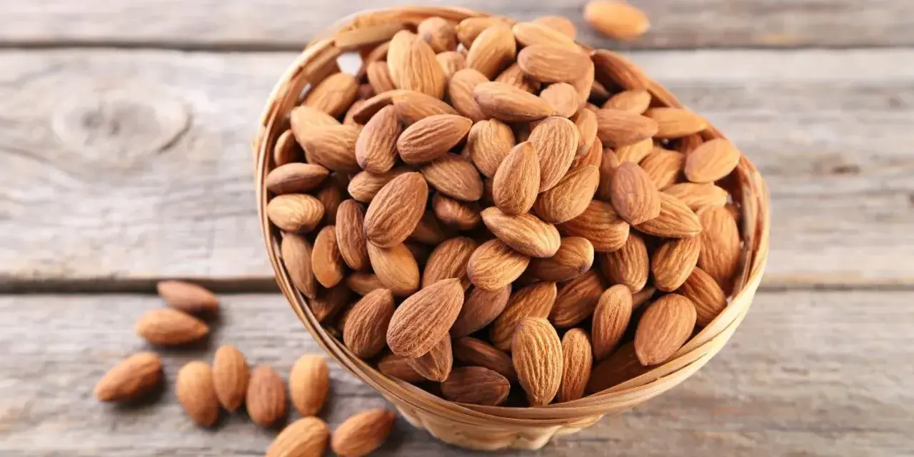 Un panier rempli d'amandes sur fond de bois. Savoir pourquoi faire tremper les amandes améliore leur digestibilité et leur saveur.