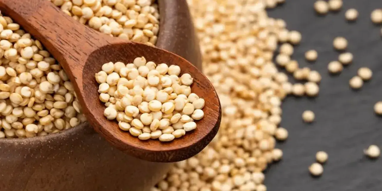 Une cuillère en bois remplie de quinoa cru, posée sur un bol débordant de ces graines nutritives.