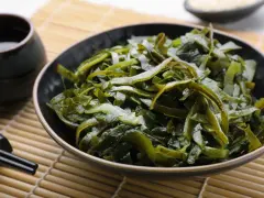 Un bol de salade d'algues kombu, aux multiples algue kombu bienfaits, servi avec une sauce et des baguettes sur un tapis de bambou.