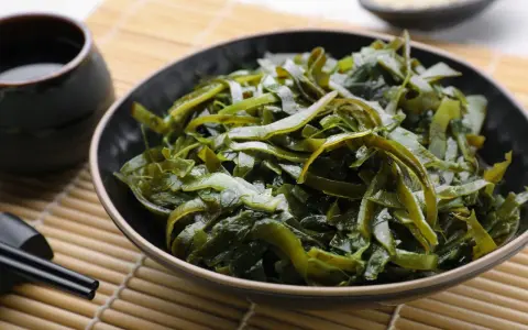 Un bol de salade d'algues kombu, aux multiples algue kombu bienfaits, servi avec une sauce et des baguettes sur un tapis de bambou.