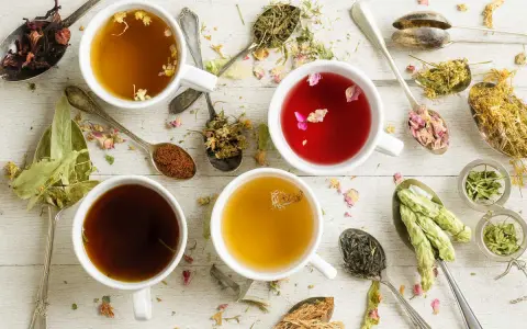 Tasses de tisanes aux herbes variées, idéales pour une infusion douleur règles. Des cuillères regorgent de fleurs séchées et de feuilles.