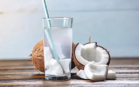 Verre d'eau de coco fraîche avec des morceaux de noix de coco. Une boisson naturelle pour soulager la constipation.