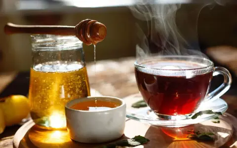 Une cuillère en bois verse du miel doré dans une tasse de thé fumante. Un délice réconfortant de miel dans eau chaude.