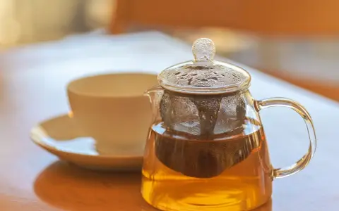 Théière en verre remplie de tisane dorée, avec une tasse en arrière-plan. La question est : combien de temps peut on garder une tisane infusée ?
