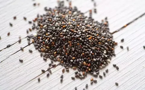 Un tas de graine de chia germé, petites et noires, sur un fond de bois blanc.