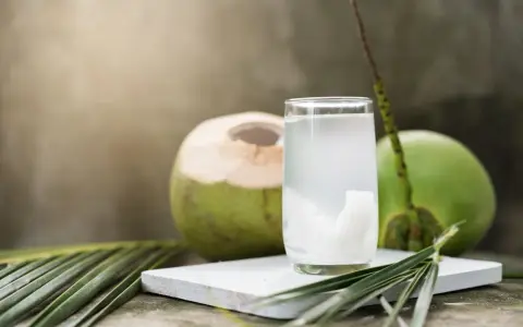 Un verre d'eau de coco, riche en potassium, à côté de noix de coco fraîches et de feuilles de palmier.
