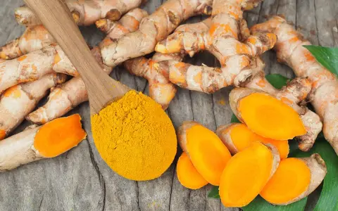 Curcuma fraîche et poudre dorée sur cuillère en bois, évoquant les nombreux curcuma frais bienfaits pour la santé.