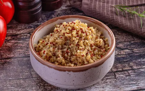 Un bol de quinoa, riche en fibres, prêt à être dégusté. Des tomates rouges et une branche de romarin complètent la scène.