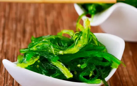 Salade d'algue de mer verte et brillante, servie dans un bol blanc, prête à être dégustée avec des baguettes.