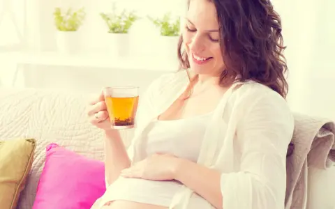 Femme enceinte souriante tenant une tasse d'infusion de thym, posant sa main sur son ventre.