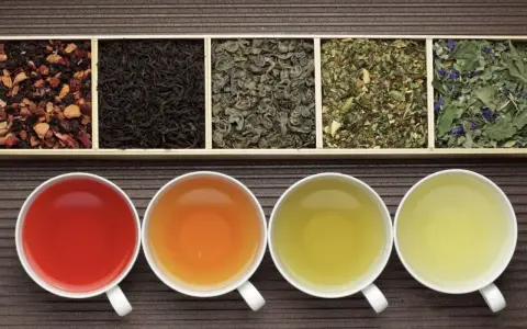 Six variétés de thés en vrac dans des compartiments, avec quatre tasses de thé infusé. Savoir combien de temps se conserve le thé en vrac est essentiel pour en apprécier la saveur.
