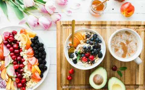 Un bol de yaourt aux fruits rouges, myrtilles et amandes, un plateau de fruits frais, un avocat et une tasse de café. Un repas sain, un aliment anti inflammatoire.