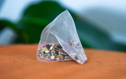 Un sachet de tisane pour anémie, rempli d'herbes et de pétales de fleurs colorés, repose sur un tissu orange.