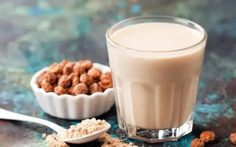 Un verre de lait de souchet crémeux, à côté d'une coupelle de tubercules et d'une cuillère de poudre.