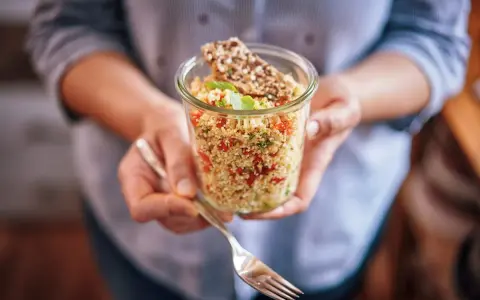 Un bocal rempli de quinoa coloré, parfait pour un régime sain. Une fourchette est prête à déguster ce plat savoureux.