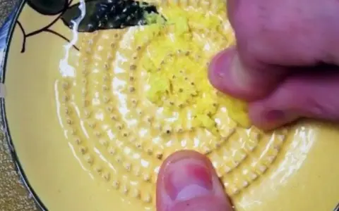 Main d'une personne râpe du gingembre sur une râpe jaune décorée.