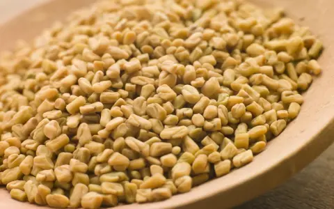 Graines de fenugrec sur une cuillère en bois, une aide naturelle pour gérer l'hypertension.
