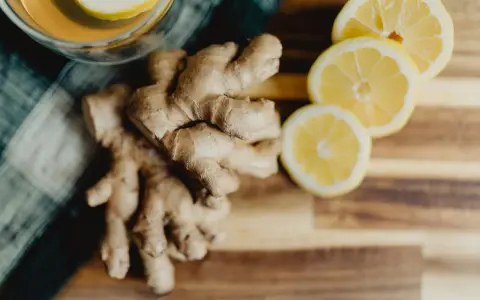 Un verre de thé avec une tranche de citron et du gingembre frais sur une planche en bois. Parfait pour boire du gingembre le matin.