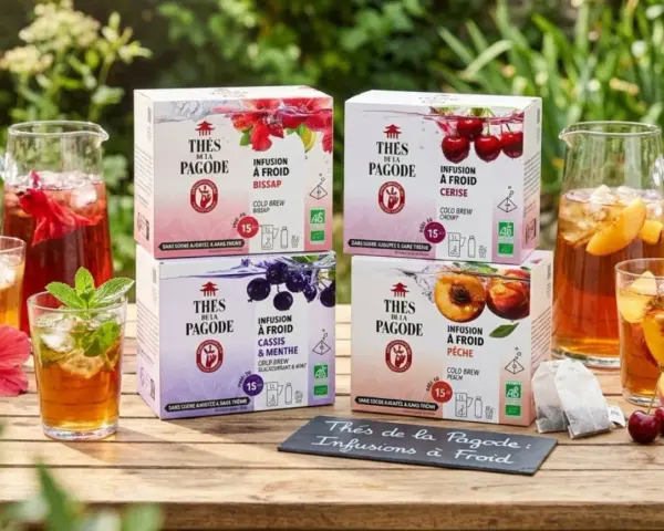 Quatre boîtes de "Thés de la Pagode" : infusions à froid Bissap, Cerise, Cassis & Menthe, et Pêche. Des carafes et verres de boissons glacées complètent la scène.