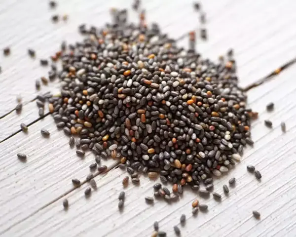 Un tas de graine de chia germé, petites et noires, sur un fond de bois blanc.