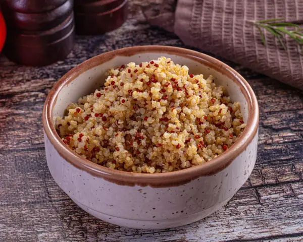 Un bol de quinoa, riche en fibres, prêt à être dégusté. Des tomates rouges et une branche de romarin complètent la scène.