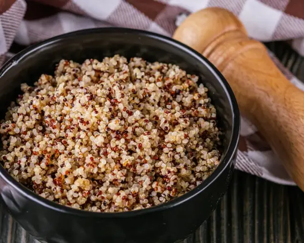 Un bol de quinoa, un aliment polyvalent, est-il un féculent ou une légumineuse ? Servi avec une serviette à carreaux et un moulin à poivre en bois.