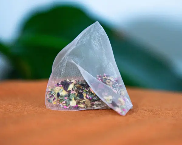 Un sachet de tisane pour anémie, rempli d'herbes et de pétales de fleurs colorés, repose sur un tissu orange.