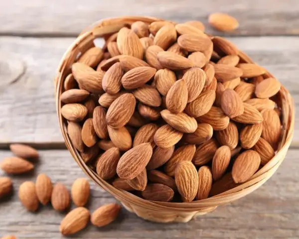 Un panier rempli d'amandes sur fond de bois. Savoir pourquoi faire tremper les amandes améliore leur digestibilité et leur saveur.