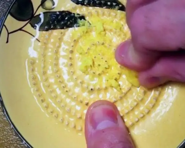 Main d'une personne râpe du gingembre sur une râpe jaune décorée.
