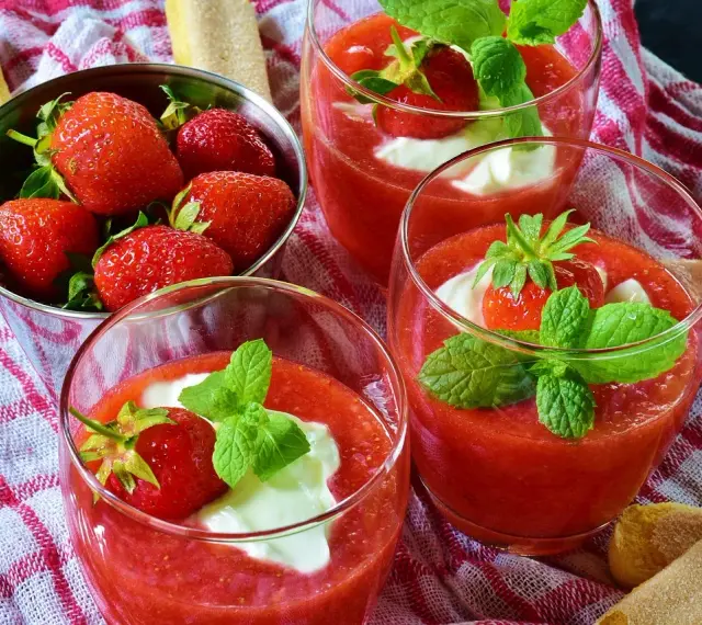 Trois coupes de coulis de fraise, garnies de crème et de menthe, avec des fraises fraîches dans un bol.