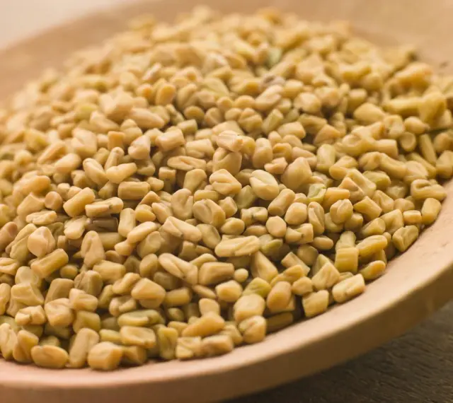 Graines de fenugrec sur une cuillère en bois, une aide naturelle pour gérer l'hypertension.