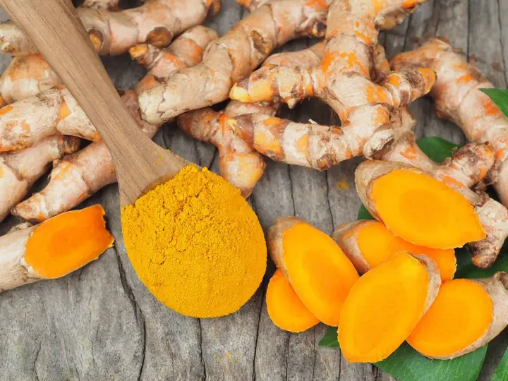 Curcuma fraîche et poudre dorée sur cuillère en bois, évoquant les nombreux curcuma frais bienfaits pour la santé.