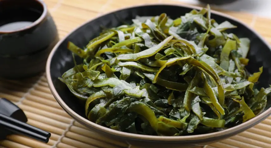 Un bol de salade d'algues kombu, aux multiples algue kombu bienfaits, servi avec une sauce et des baguettes sur un tapis de bambou.
