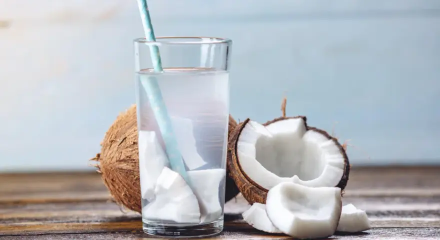 Verre d'eau de coco fraîche avec des morceaux de noix de coco. Une boisson naturelle pour soulager la constipation.