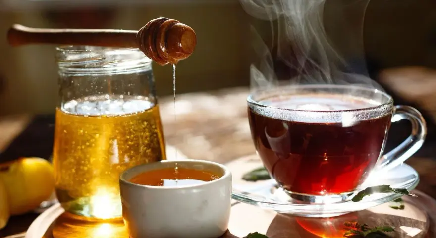 Une cuillère en bois verse du miel doré dans une tasse de thé fumante. Un délice réconfortant de miel dans eau chaude.