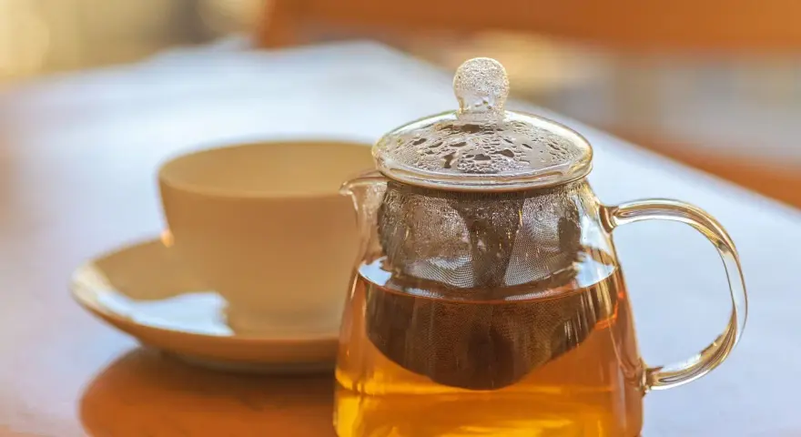 Théière en verre remplie de tisane dorée, avec une tasse en arrière-plan. La question est : combien de temps peut on garder une tisane infusée ?