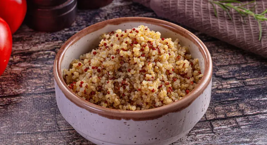Un bol de quinoa, riche en fibres, prêt à être dégusté. Des tomates rouges et une branche de romarin complètent la scène.