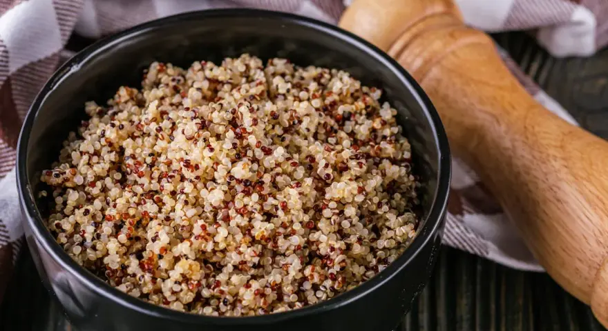 Un bol de quinoa, un aliment polyvalent, est-il un féculent ou une légumineuse ? Servi avec une serviette à carreaux et un moulin à poivre en bois.