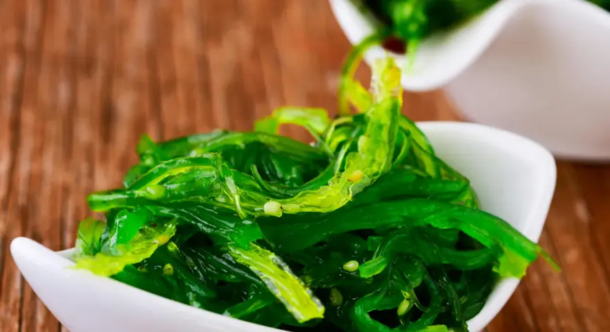 Salade d'algue de mer verte et brillante, servie dans un bol blanc, prête à être dégustée avec des baguettes.